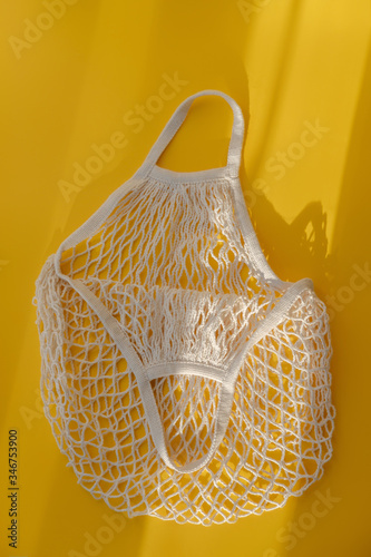 Empty mesh string bag on bright yellow background and hard sunshine. The concept of zero waste. Using reusable bags instead of disposable cellophane packets.