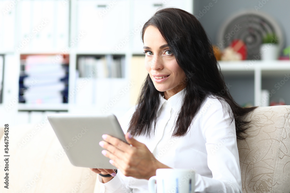 Woman sitting on sofa and makes notes on laptop