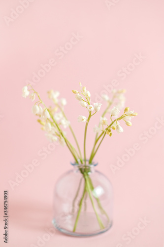 Greeting card with white lily of the valley on pink background for celebration Mothers Day, wedding, March 8. Nature concept. Home garden in vase. Summer green floral design. Selective focus.