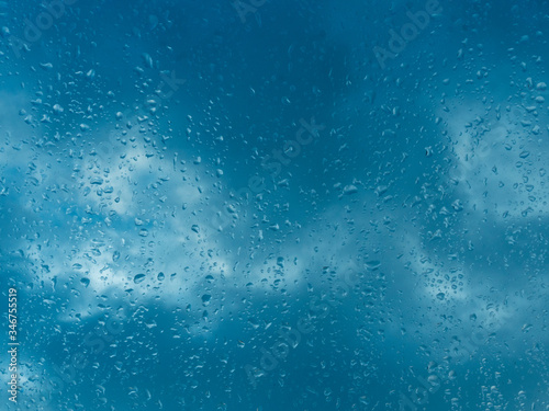 Wet blue window with rain drops and a cloudy sky outside.
