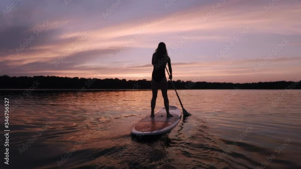 Girl stroking away on her stand up paddle board into the sunset