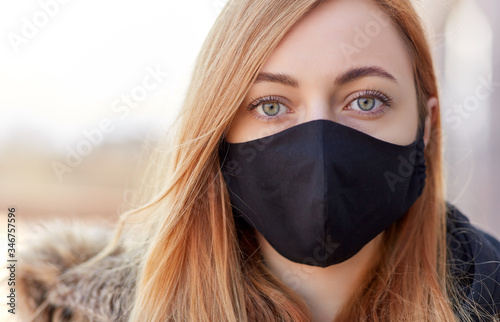 health, safety and pandemic concept - young woman wearing black face protective reusable barrier mask outdoors photo