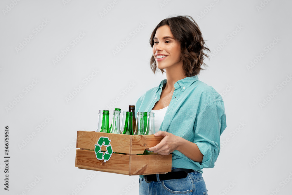 recycling, waste sorting and sustainability concept - smiling young woman holding wooden box with glass bottles and jars over grey background recycling, waste sorting and sustainability concept - smiling young woman holding wooden box with glass bottles and jars over grey background