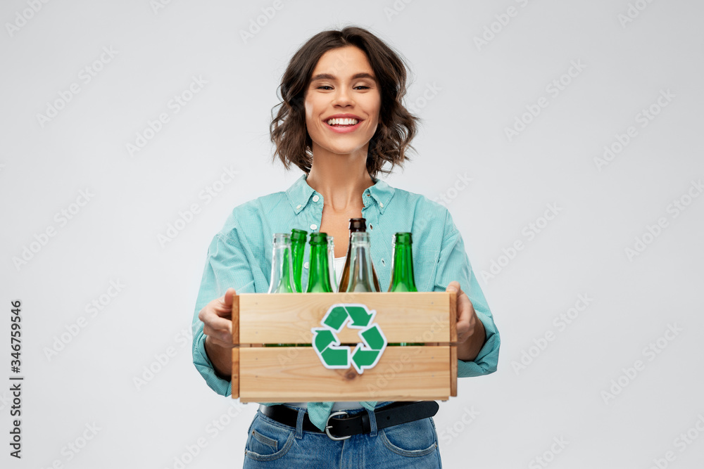recycling, waste sorting and sustainability concept - smiling young woman holding wooden box with glass bottles and jars over grey background recycling, waste sorting and sustainability concept - smiling young woman holding wooden box with glass bottles and jars over grey background
