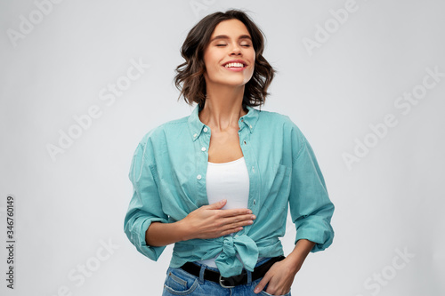 digestion, eating people concept - happy smiling full young woman in turquoise shirt touching her tummy over grey background photo