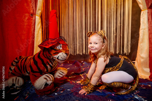 Little girl dressed in a costume with ears and tail poses in stylized theatrical circus photo shoot with a toy tiger