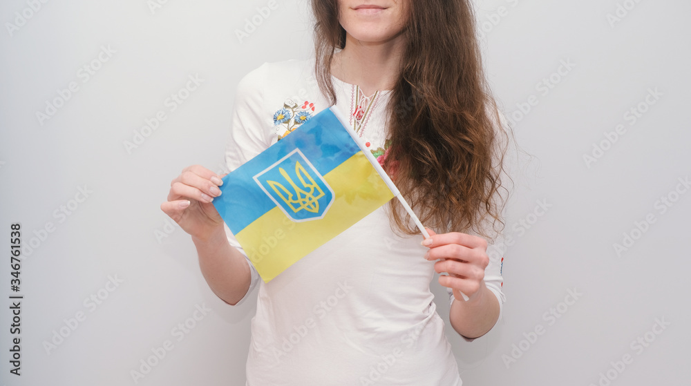 Young beautiful girl in embroidered shirt with Ukrainian flag. Attractive Ukrainian woman wearing traditional Ukrainian embroidery on the grey background. Young beautiful girl in embroidered shirt with Ukrainian flag. Attractive Ukrainian woman wearing traditional Ukrainian embroidery on the grey background.