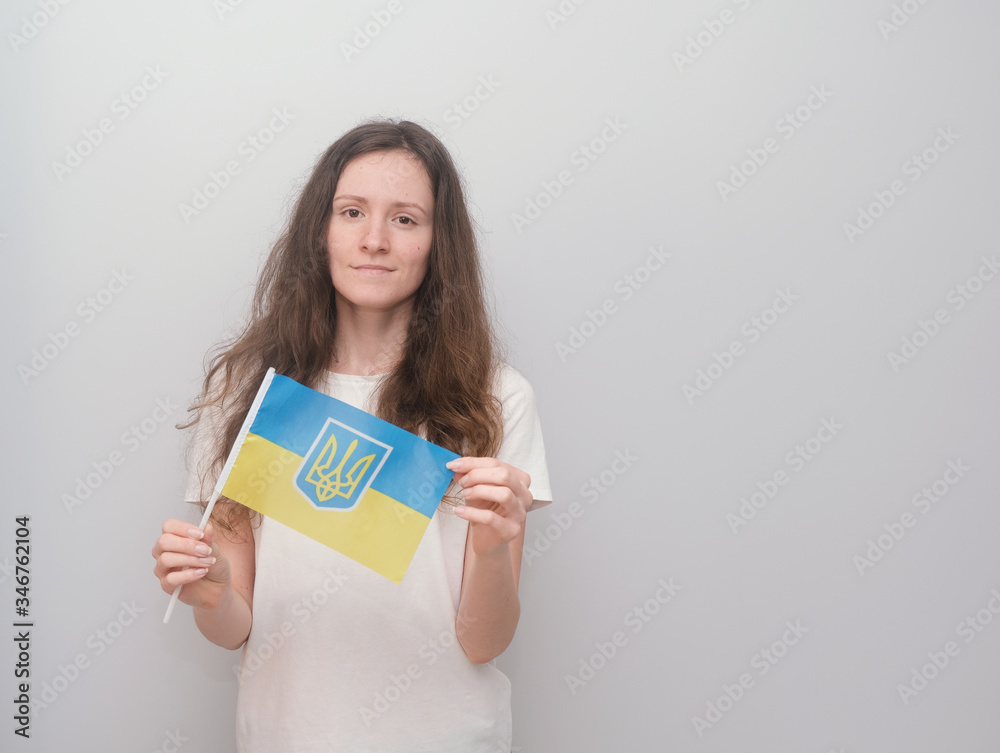 Happy girl holding Ukrainian flag on the grey background.
