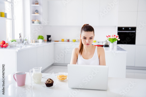 Photo of domestic charming house wife lady sitting morning kitchen browsing notebook freelancer drink tea milk have breakfast staying home distance remote work quarantine time indoors