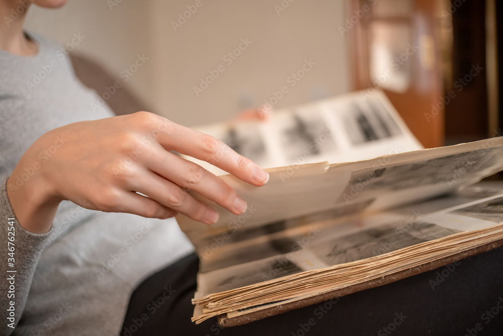girl in a gray jacket holds an old photo album with black and white photos on her lap and looks at them sitting on the sofa girl in a gray jacket holds an old photo album with black and white photos on her lap and looks at them sitting on the sofa
