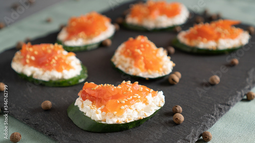 Sandwiches with cucumber at the base, cream cheese and salmon on top on a black tray. Healthy alternative
