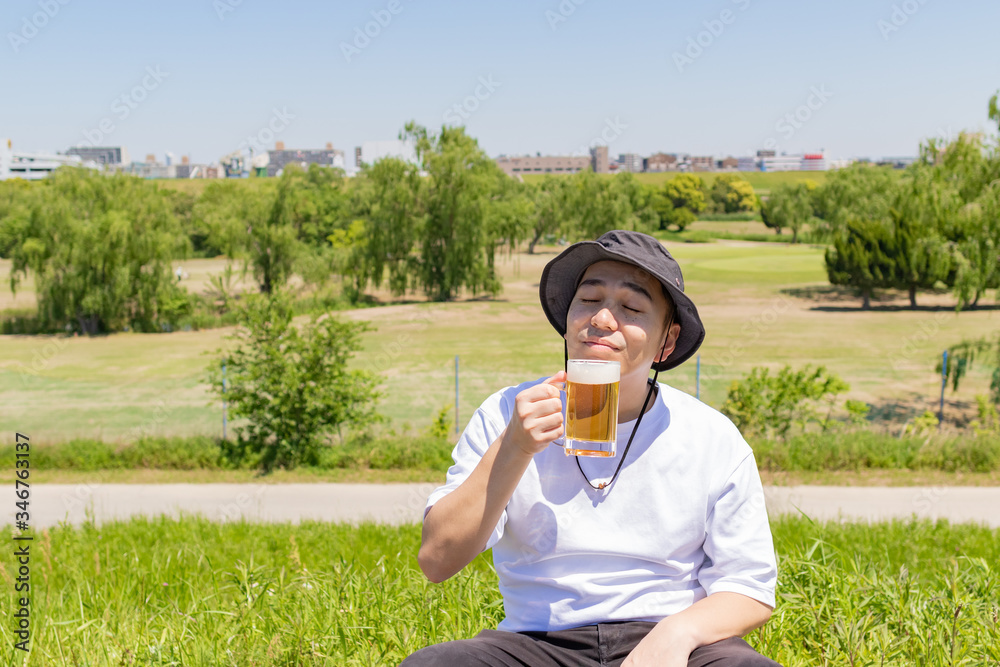 Fototapeta premium 屋外でビールを飲む日本人男性。青空背景