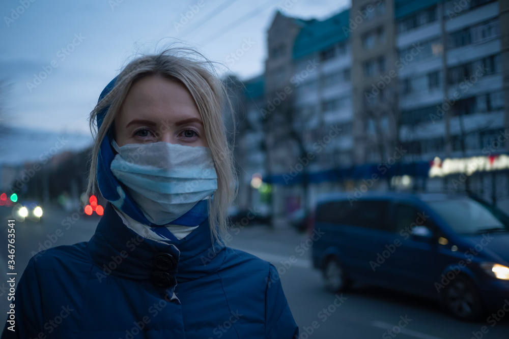young blonde woman with a stole on her head in a medical mask close-up on a street in the city. Prevention of the spread of the flu virus.