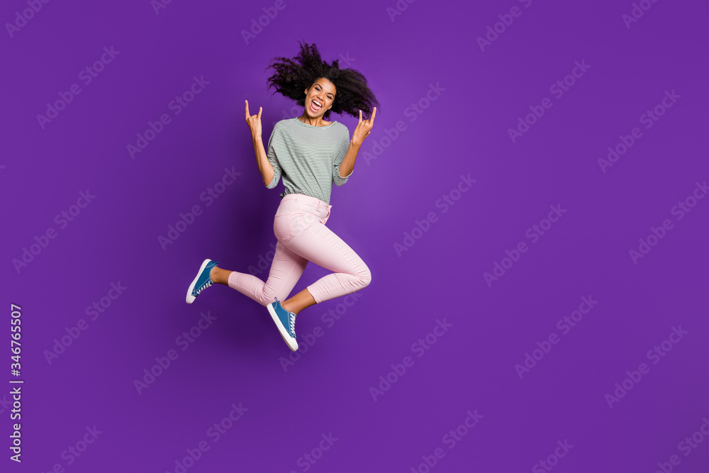 Full length photo of crazy funky afro american girl rocker jump show horne sign enjoy pank concert wear striped shirt pink clothing isolated over purple color background