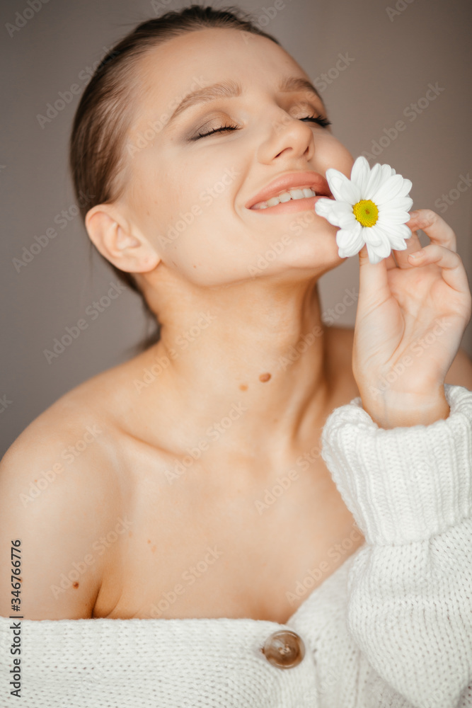 Lovely girl with closed eyes in a white sweater brings a white flower to her lips Lovely girl with closed eyes in a white sweater brings a white flower to her lips