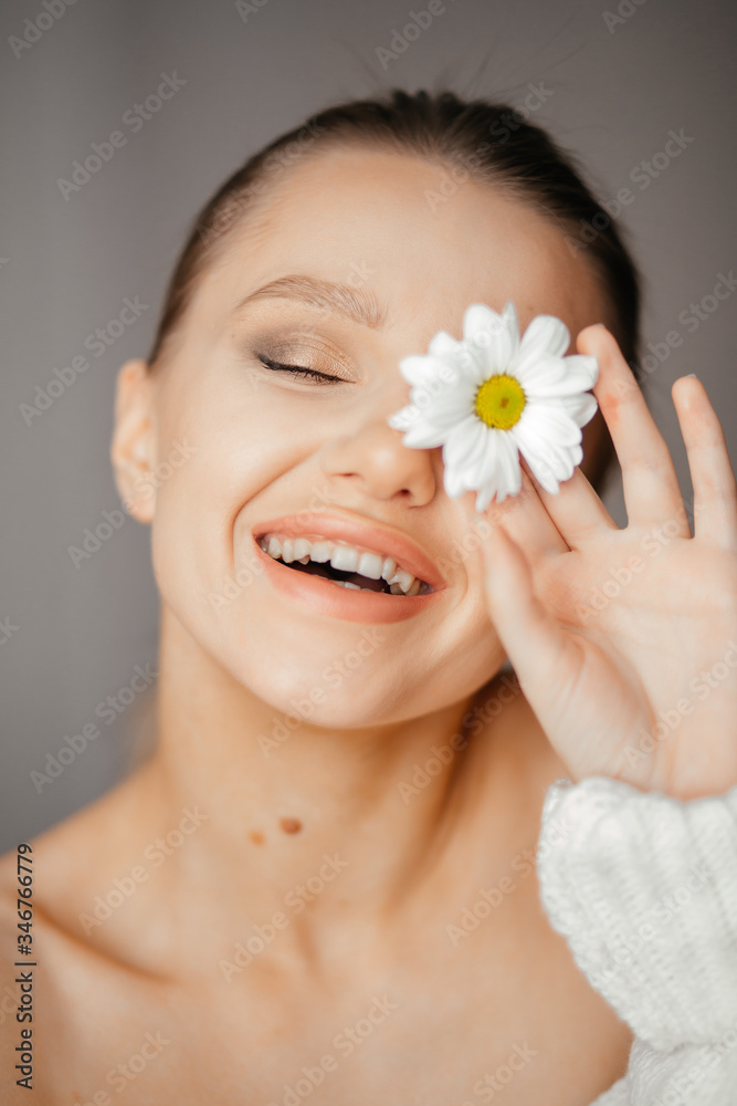 Lovely girl with closed eyes in a white sweater brings a white flower to her eye Lovely girl with closed eyes in a white sweater brings a white flower to her eye