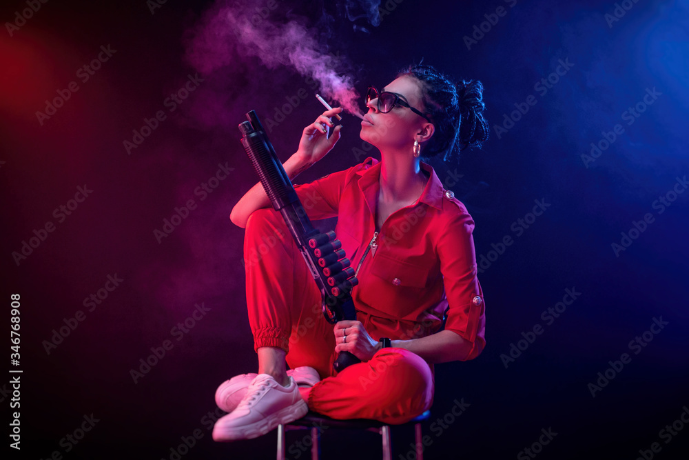 a bright brunette in a red jumpsuit with a shotgun on a dark background in neon light