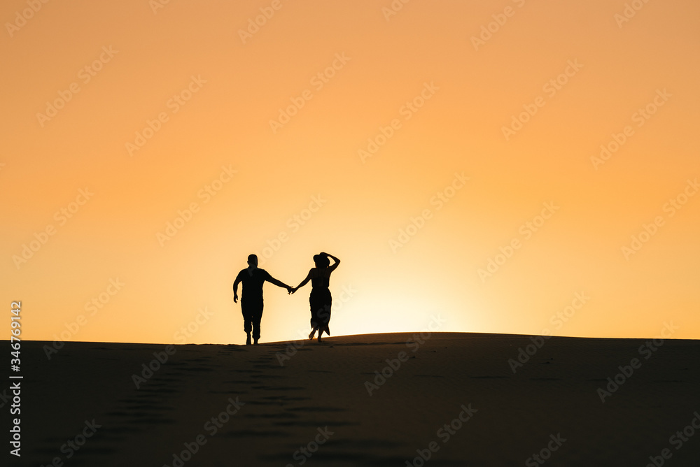 silhouettes of a happy young couple on a background of orange sunset in the sand desert