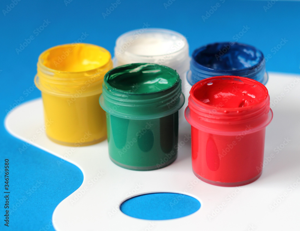 Containers of watercolor paints and white paintbrushes palette on blue background. Containers of watercolor paints and white paintbrushes palette on blue background.