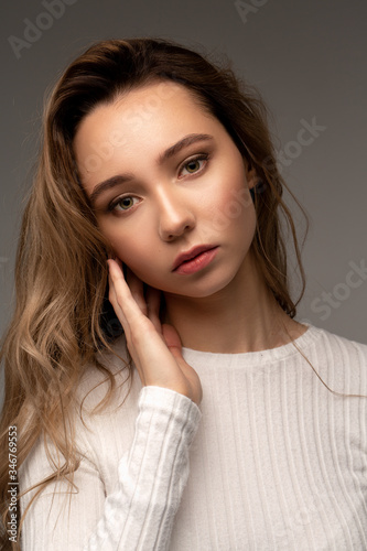 Beautiful portrait of young model with curly hair on grey background in white shirt