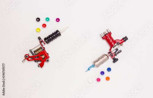 Rotary and induction tattoo machines and color paints in disposable plastic jars on a white background. Free space for text. The view from the top.