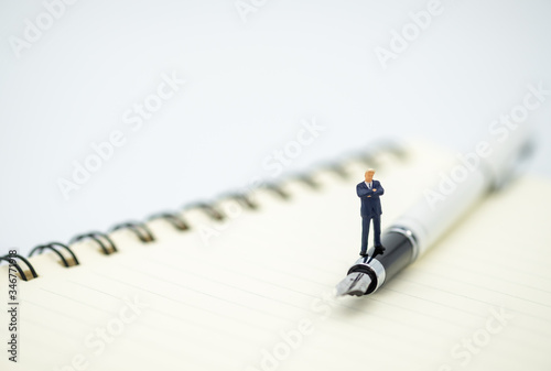 A figure miniature businessman  stands on pen and note book with white background and copy space. Using as business, financial, money and cooperation concept.