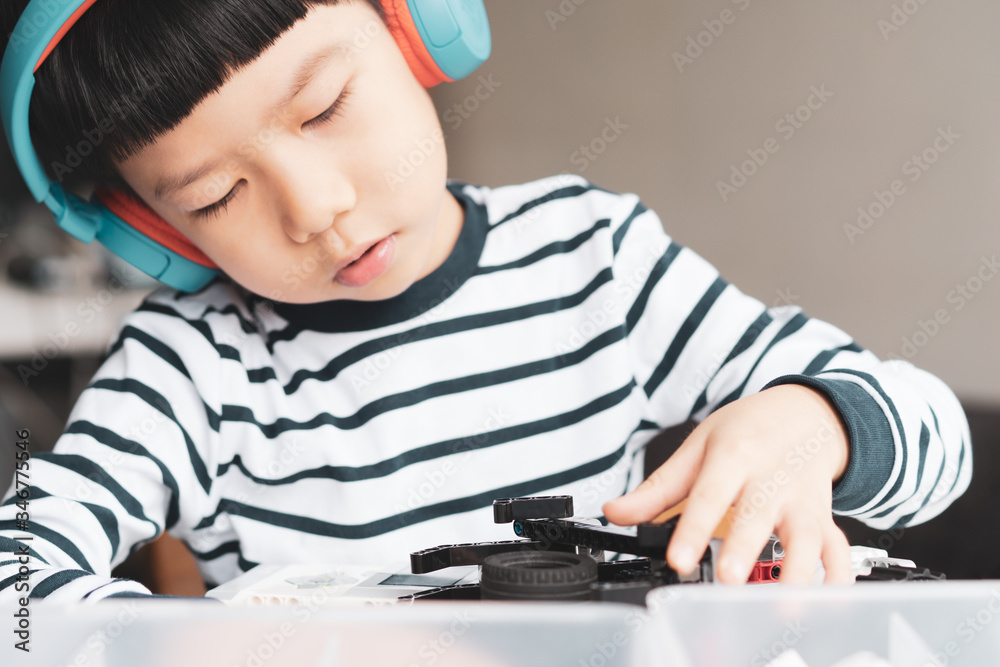 Social distancing & Learning activities, Young primary student Asian boy with blue headphone assemble a robot with EV3 components for school project at home due to school closed and Covid-19 pandemic Social distancing & Learning activities, Young primary student Asian boy with blue headphone assemble a robot with EV3 components for school project at home due to school closed and Covid-19 pandemic