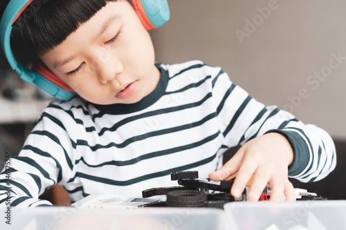 Social distancing & Learning activities, Young primary student Asian boy with blue headphone assemble a robot with EV3 components for school project at home due to school closed and Covid-19 pandemic