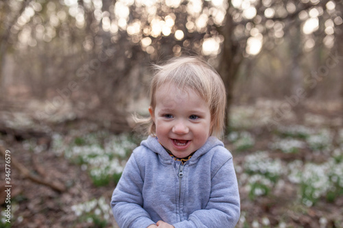 Little pretty girl in a clearing of snowdrops. A child walks in the spring forest.