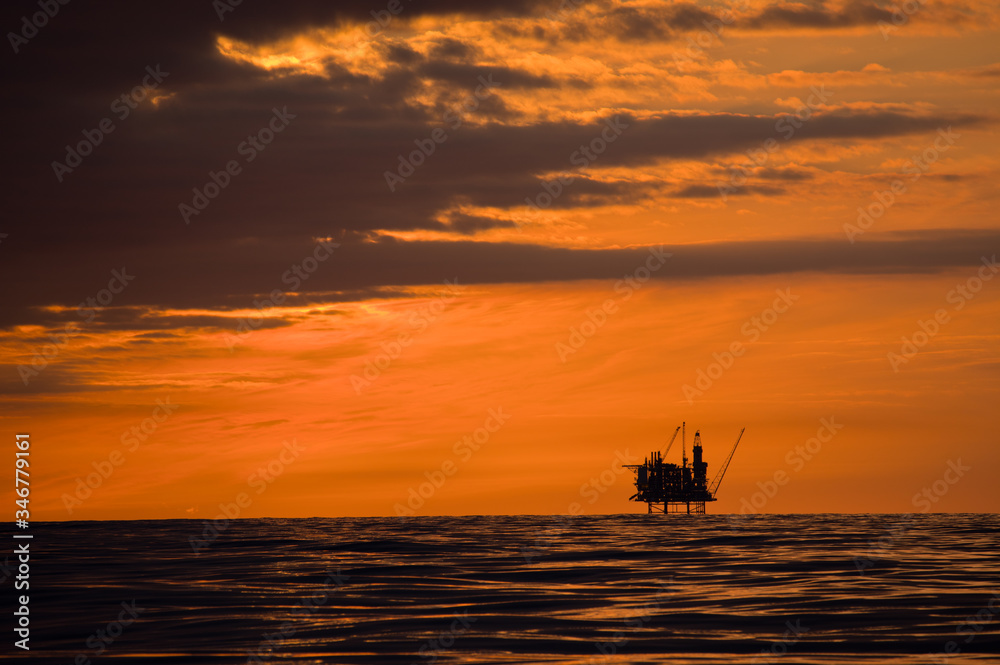 A production platform in the North Sea halfway between Utsira and Inverness. Colorful sunset, sky partly covered by dark clouds - calm sea in July. Rig photographed against the light.