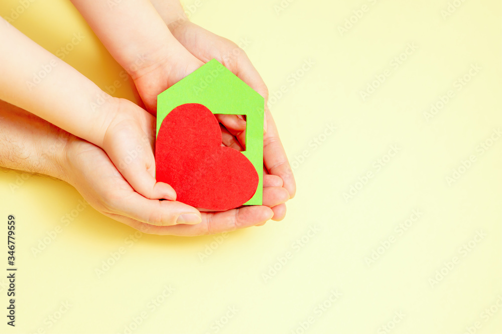 Hands of child and dad holding paper heart with house on yellow background. Family home concept. Picture with copy space. Hands of child and dad holding paper heart with house on yellow background. Family home concept. Picture with copy space.