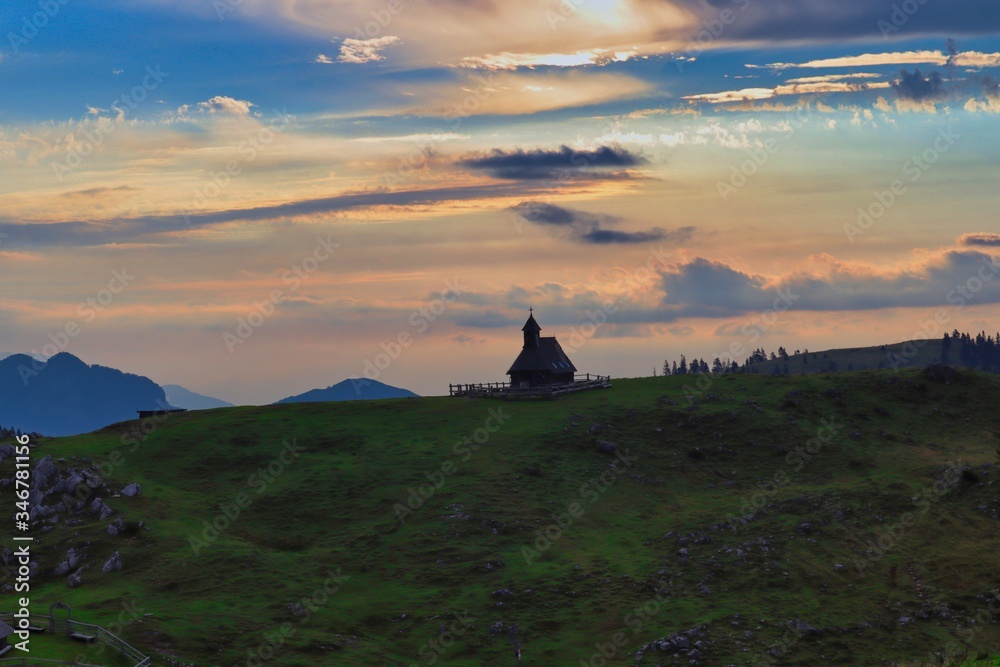 Little church in Velika Planina. Christian church in Big Pasture Plateau with sunrise colorful sky and beautiful mountain silhouettes in the background.