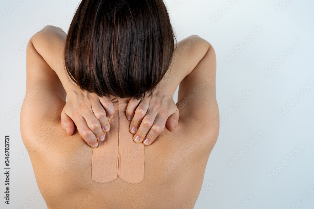 Kinesiology beige taping on the human back on a gray background with a copy space. Dynamic functional bandage taping on the girl's neck. Solution for back and neck pain. Headache.