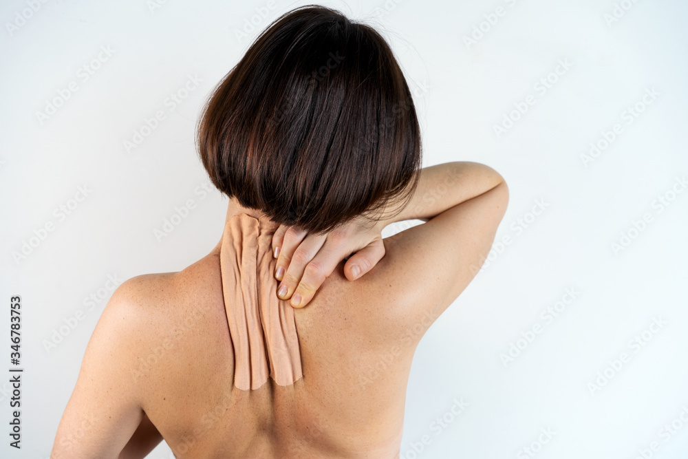Kinesiology beige taping on the human back on a gray background with a copy space. Dynamic functional bandage taping on the girl's neck. Solution for back and neck pain. Headache. Kinesiology beige taping on the human back on a gray background with a copy space. Dynamic functional bandage taping on the girl's neck. Solution for back and neck pain. Headache.