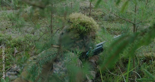 Soldier in the woods under tree getting in to position to shoot with rifle photo