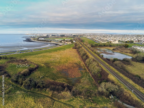 Fototapeta Naklejka Na Ścianę i Meble -  Aerial view on rail road to Galway city, Ireland,  empty Ballyloughane beach, Cloudy sky. Rails act as leading line to town.