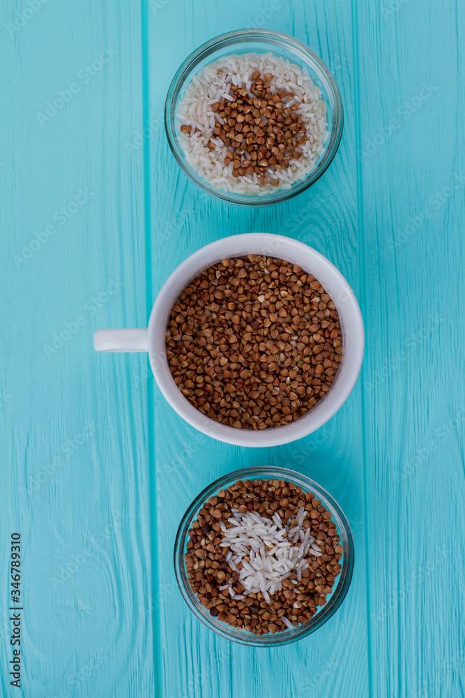Three cups with buckwheat and rice on blue wood. View from above. Three cups with buckwheat and rice on blue wood. View from above.