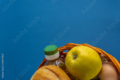 Donation, alms, healthy nutrition, humanitarian aid, pandemic, Covid-19 concept. Flatlay omposition of food in a wicker wooden basket on a blue background, copy space. photo