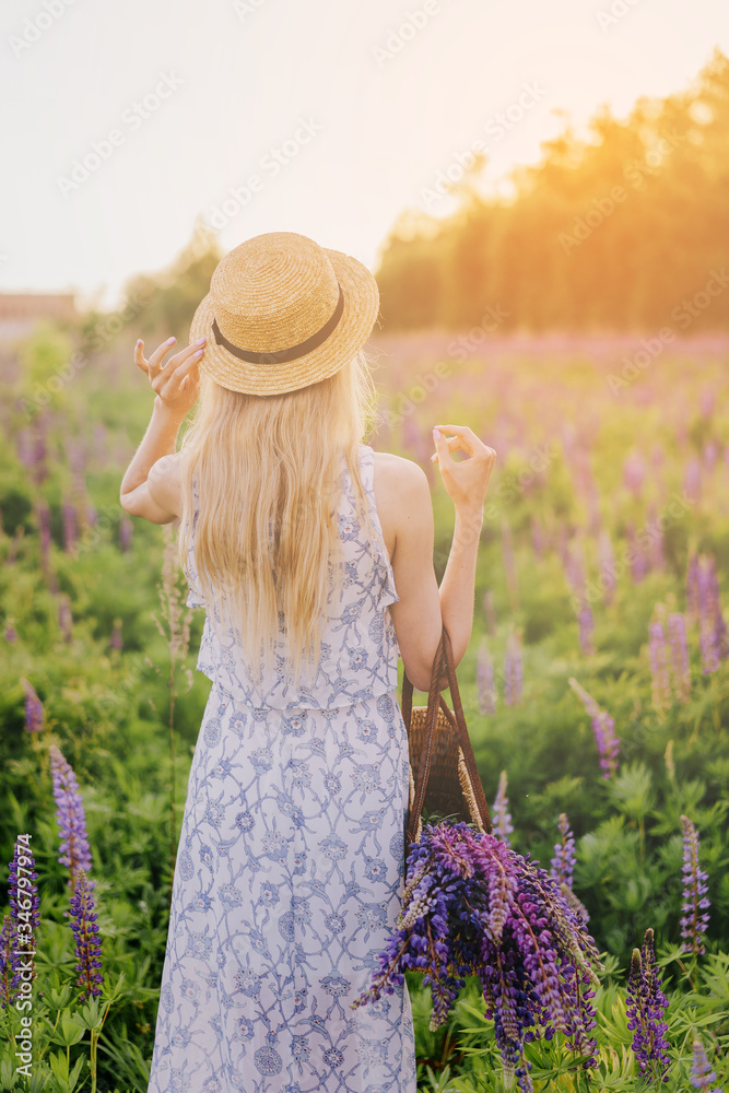 Φωτογραφία Young blonde girl with long hair in summer dress and a wicker hat with a ribbon