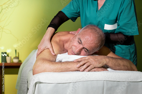 Uomo anziano in completo relax si fa massaggiare su un lettino da una massaggiatrice professionista in un centro massaggi photo