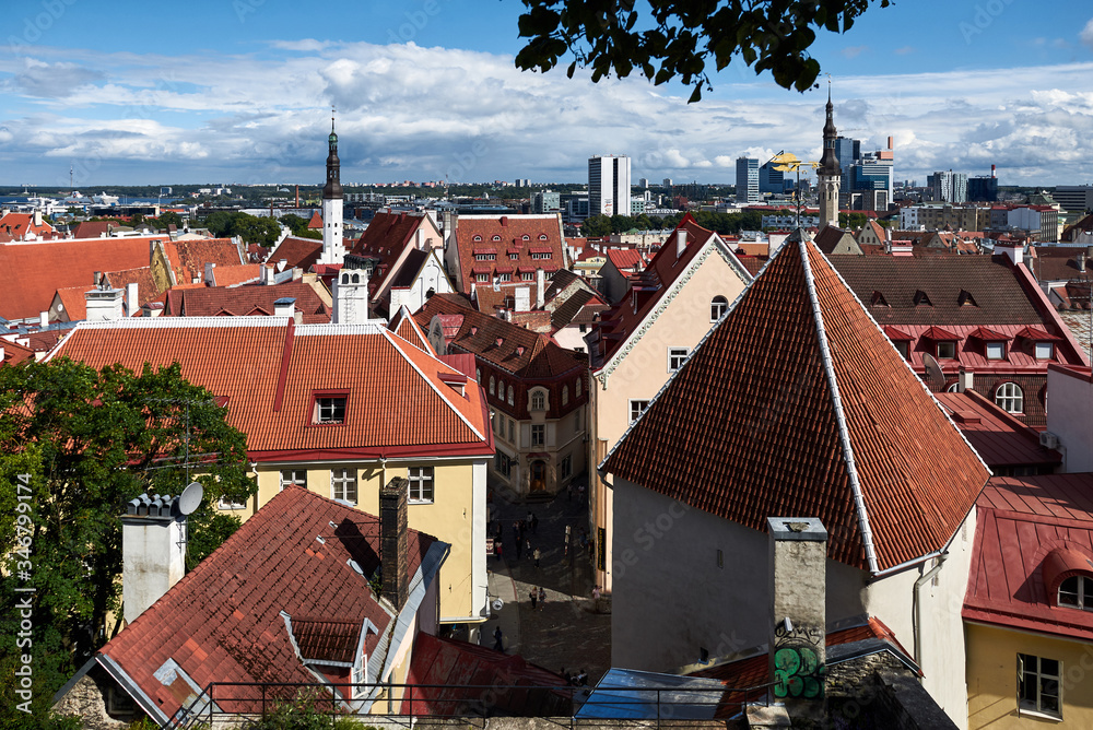 Red tile roofs of the old center of a European city. in the distance a new city is visible. sunny weather with blue sky and clouds, shadows and sun glare fall on streets and houses