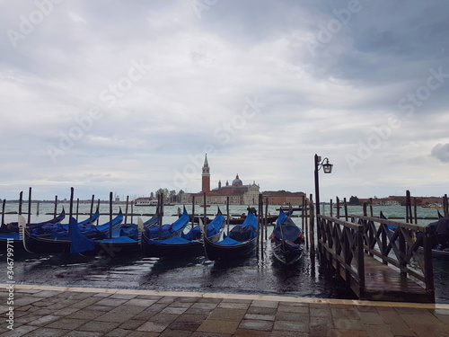 Gondolas on the pier of the Venetian canal under a cloudy sky