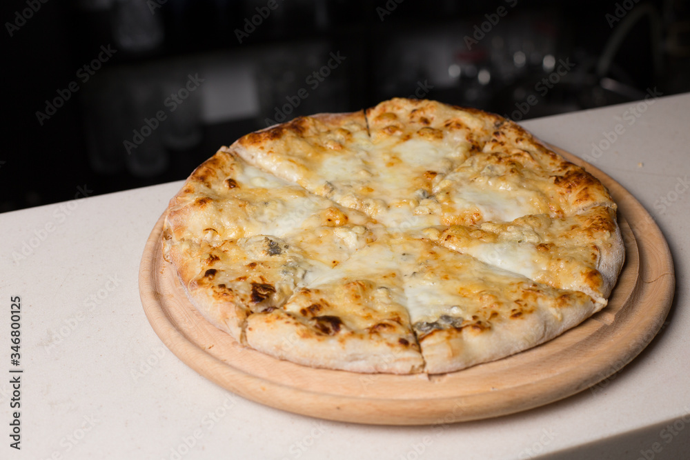 four cheese pizza on a wooden plate in a bar