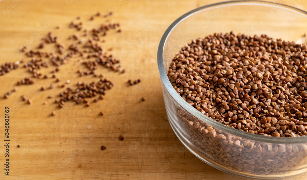 raw buckwheat in a transparent deep bowl. seeds are scattered carelessly nearby. kitchen table. daylight raw buckwheat in a transparent deep bowl. seeds are scattered carelessly nearby. kitchen table. daylight