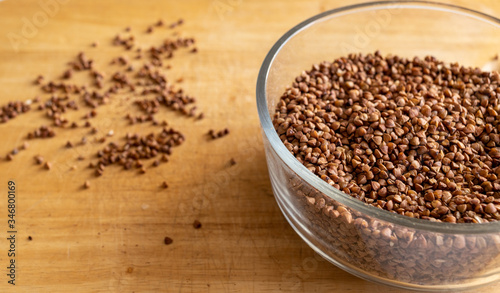 raw buckwheat in a transparent deep bowl. seeds are scattered carelessly nearby. kitchen table. daylight