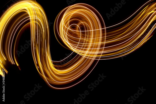 Long exposure photograph of neon gold colour in an abstract swirl, parallel lines pattern against a black background. Light painting photography.