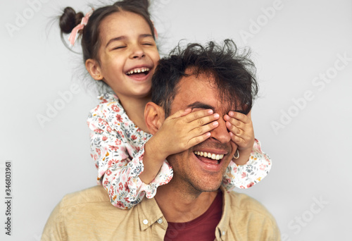 Closeup image of smiling little girl embraces her dad, shares love together. Handsome man playing with kid peekaboo game. Playful daughter cover the eyes with hands of her father for a surprise. photo