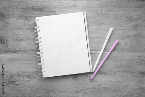 White notebook, two pens on a white wooden table top view of flat objects