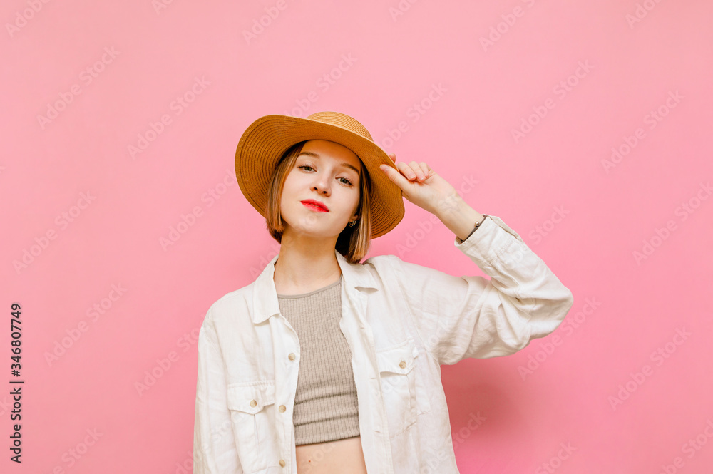 Portrait pretty girl in summer clothes isolated on pink background, looking into camera and smiling. Positive lady tourist in hat and shirt stands against pastel wall background.Copy space Portrait pretty girl in summer clothes isolated on pink background, looking into camera and smiling. Positive lady tourist in hat and shirt stands against pastel wall background.Copy space