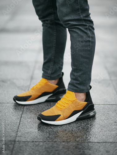 Black and yellow sneakers with white elements on legs on the street with reflection after the rain